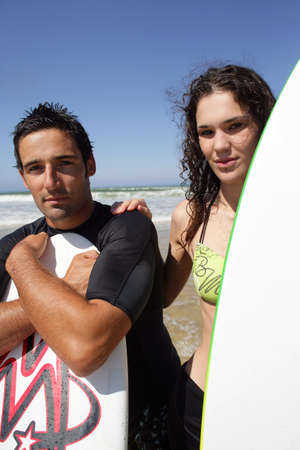 Young surfer couple stood on the beach with their surfboardsの写真素材