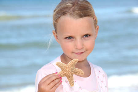 Young girl holding a starfish on the beachの写真素材