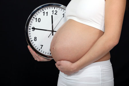 A pregnant woman holding a clock 