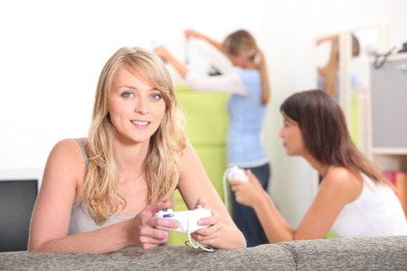 Two female friends playing video games with other friend in backgroundの写真素材