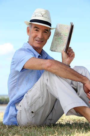 old man sitting in the grass reading an old notebookの写真素材