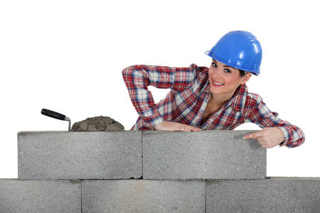 portrait of young female bricklayer pointing at concrete wallの写真素材