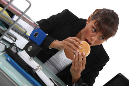 Woman eating burger at deskの写真素材