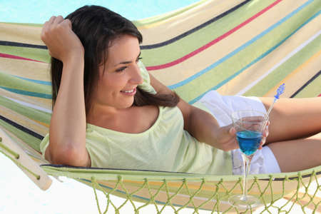Woman drinking cocktail whilst lying on hammockの写真素材