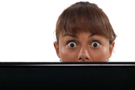 Wide-eyed woman peering over her laptopの写真素材