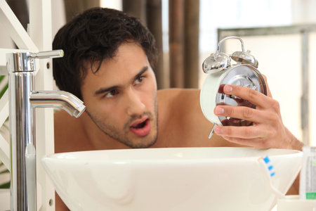 Man in bathroom shocked by how late it isの写真素材