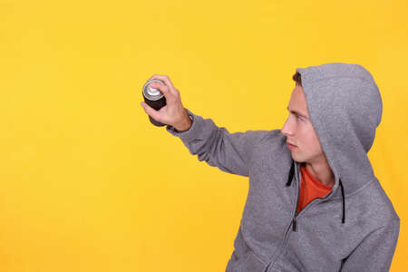 teenager wearing hoodie against yellow background holding sprayの写真素材