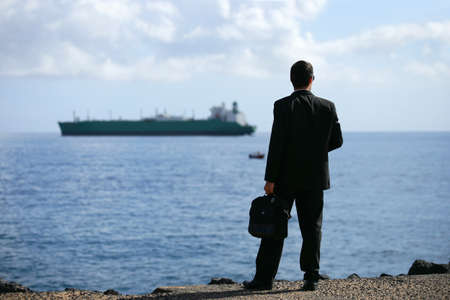 Businessman staring at a tanker out at seaの写真素材