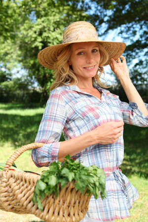 Woman holding straw hat and basket of vegetables.の写真素材