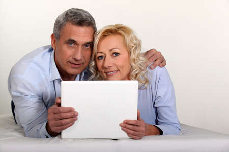 Middle aged couple with a laptop on their bed.の写真素材