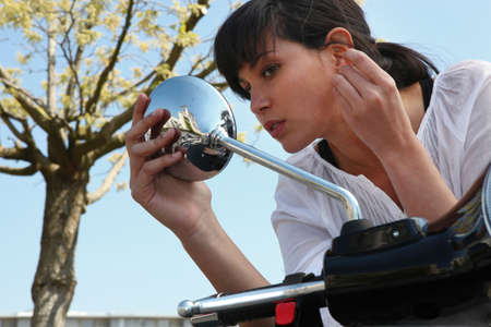 Woman looking in rearview mirror of a scooterの写真素材
