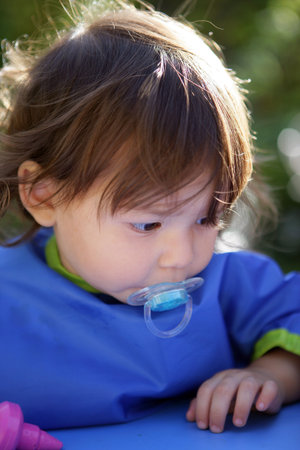 Little girl sucking on pacifier in the garden