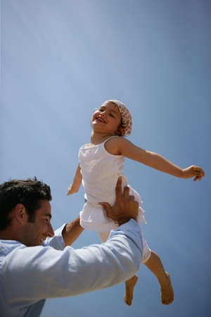 Father lifting his daughter against a blue skyの写真素材