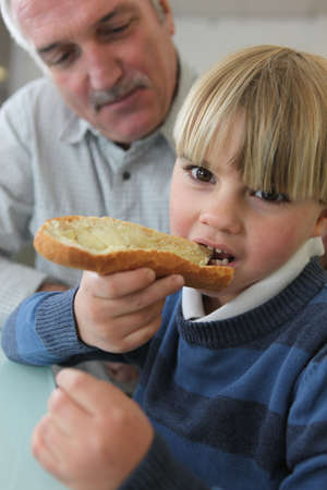 Boy eating bread with his grandfatherの写真素材