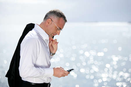 Businessman sending a text message by the seasideの写真素材