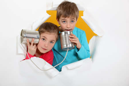 Brother and sister speaking into tin canの写真素材