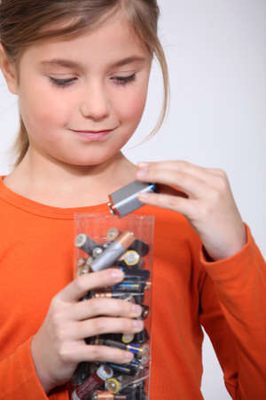 Young girl putting used batteries in a plastic containerの写真素材