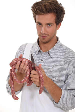 Young butcher cutting sausages on white backgroundの写真素材