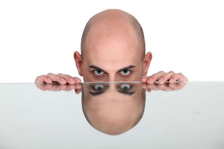 Bald man resting head on reflective surfaceの写真素材