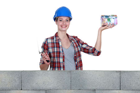 Female in mason clothing holding a house-shaped piggy bankの写真素材