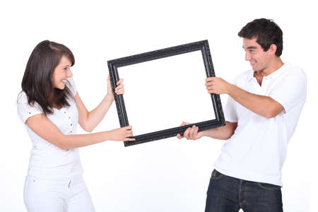 Couple fighting over blank picture frameの写真素材