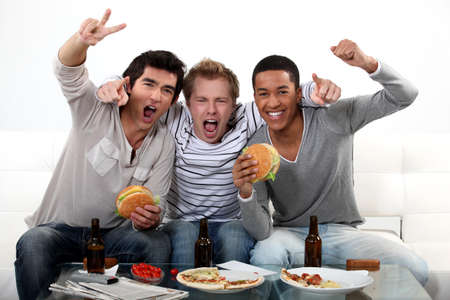 three friends eating while watching televisionの写真素材