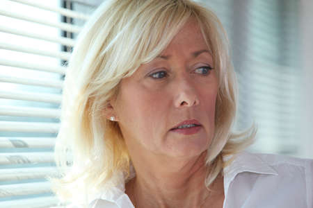 Senior businesswoman stood by window blindsの写真素材