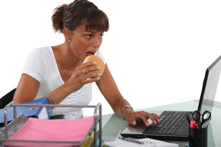Woman eating a burger at her deskの写真素材