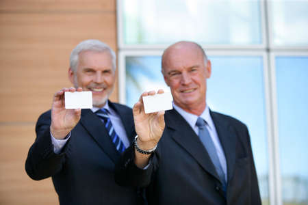 Two senior businessmen showing cardsの写真素材