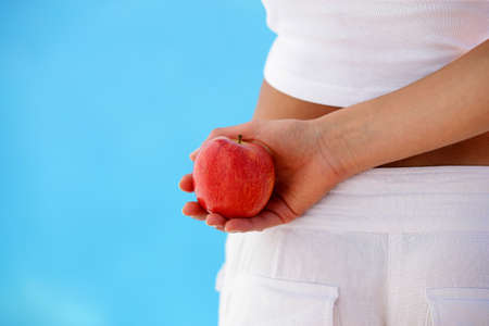 Woman holding an apple behind her backの写真素材