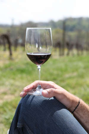 Man resting glass of wine on knee in fieldの写真素材
