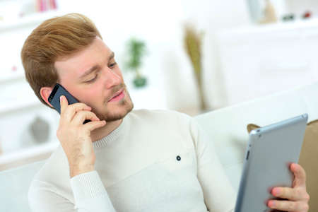 Man making a call whilst using his tablet computerの写真素材