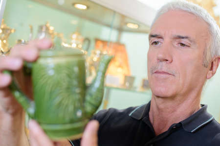 Man looking at antique tea potの写真素材