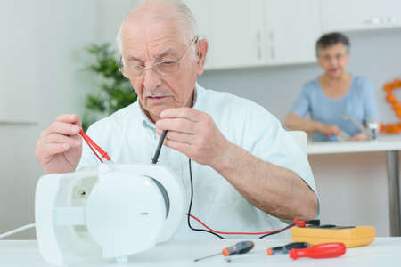 Elderly man using multi meter on electrical applianceの写真素材