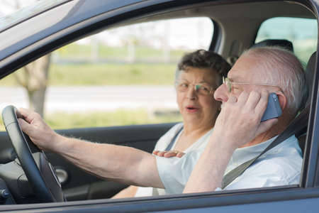 Elderly man on telephone while driving, wife in passenger seatの写真素材