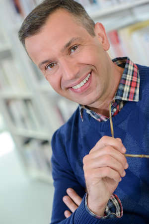 Portrait of man in library holding spectaclesの写真素材