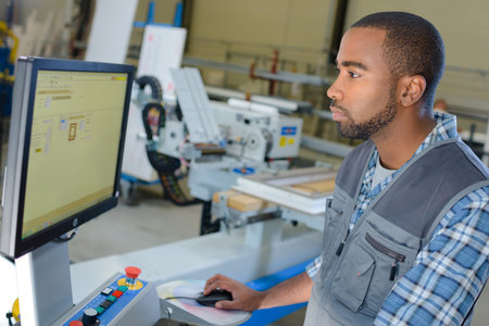 Man operating computer in industrial settingの写真素材