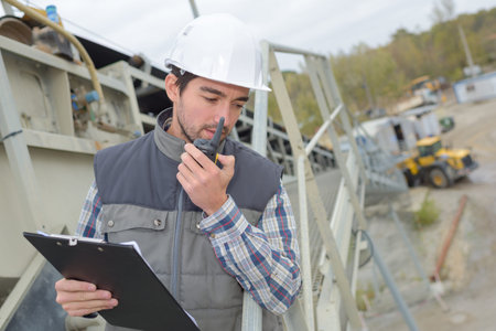 Man in construction site with clipboard and walkie talkie