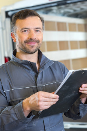 delivery man with parcels and clipboard against truckの写真素材