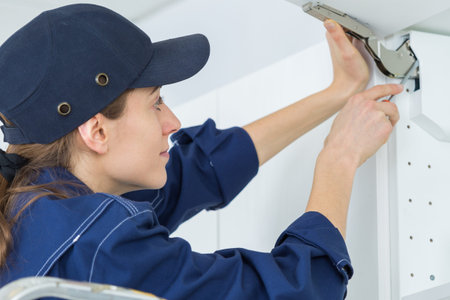 young female electrician installing electrical socket on wall with screwdriver