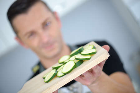 man showing sliced cucumber laying on a wooden chopping boardの写真素材