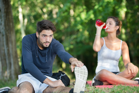 couple stretching outdoors while drinking waterの写真素材