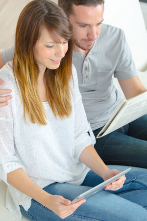 young couple reading ebooks on sofa at home