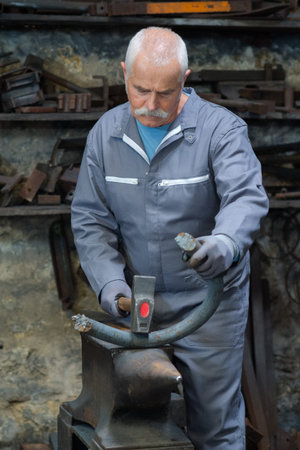 senior blacksmith forging metal on the anvil