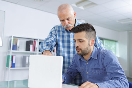 Senior man training man on computer