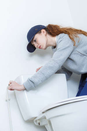 confident woman repairing toilet in bathroom at homeの写真素材