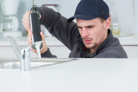 young handyman applying silicone sealant with gun around sink