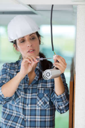 female technician installing camera on wall with screwdriverの写真素材