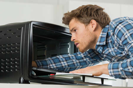 young male repairman fixing oven in kitchenの写真素材