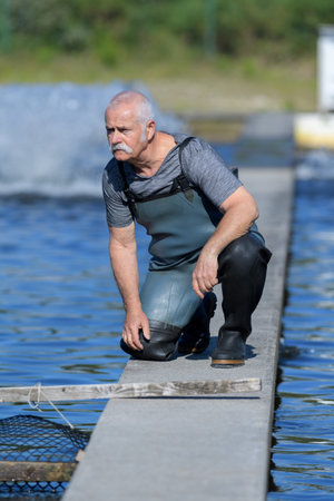 fisherman with rubber boots working at fish farm